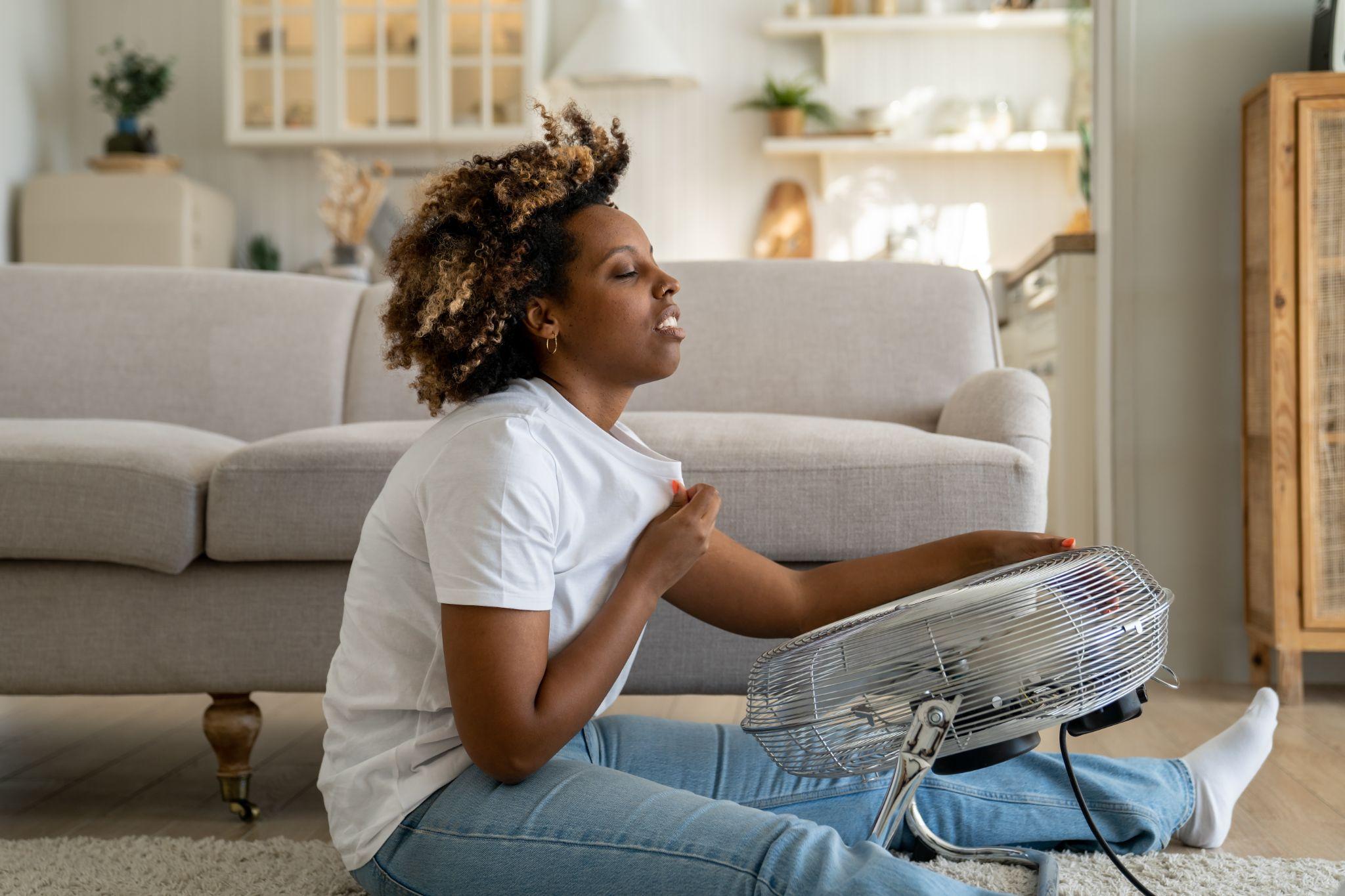 woman cooling off in front of a fan during a hot flash - perimenopause and menopause symptoms